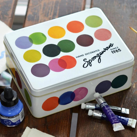 Colorful  paint dot tin with Spongeware branding on a wooden surface with paint supplies.