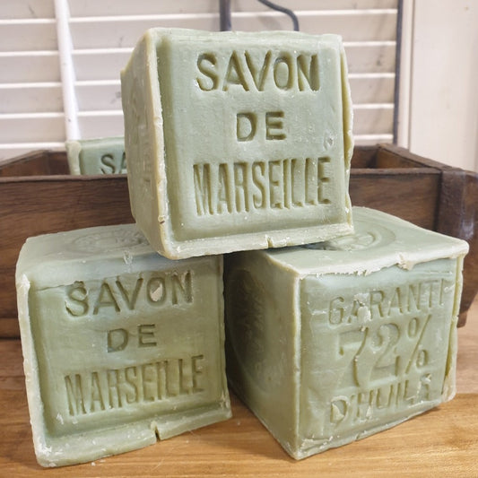 Three blocks of Marseille soap with 'SAVON DE MARSEILLE' engraved on them, displayed on a wooden surface.